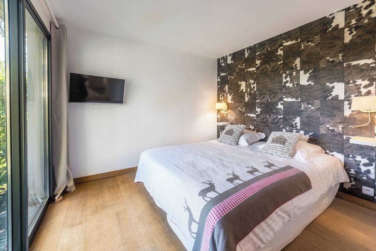 A bedroom with a bed, a mounted TV, and a patterned wall.