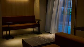 A dimly lit room with a bench, a small table, and a view through a window with curtains.