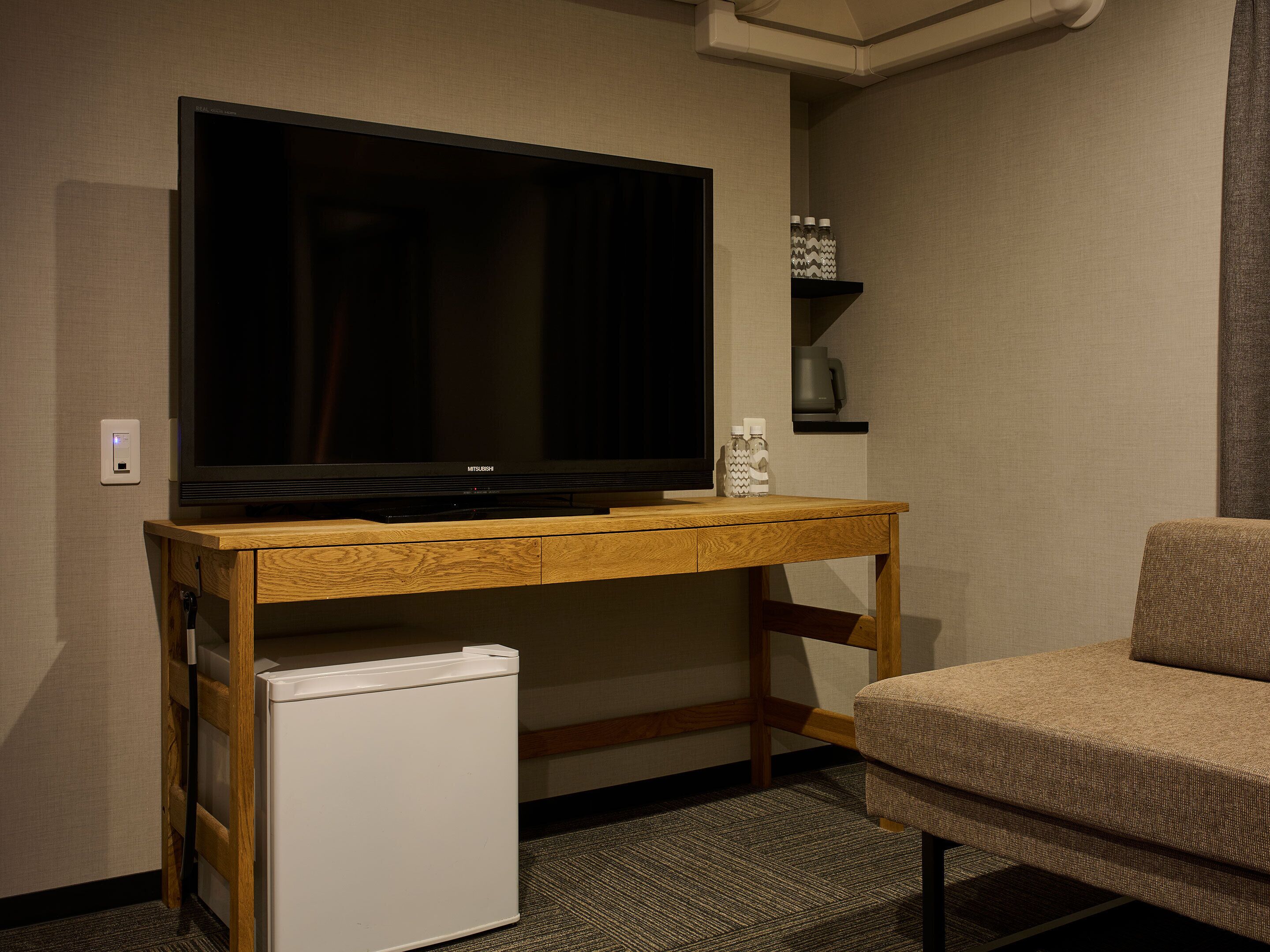 A room with a television on a wooden stand, a small white refrigerator, and a beige sofa.