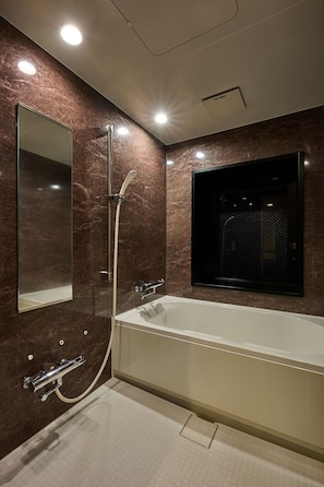 Ein modernes Badezimmer mit einer großen Badewanne, einem wandmontierten Spiegel und einer Duschbrause.
