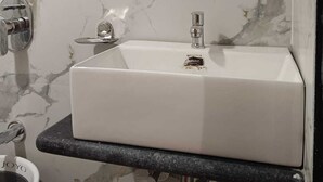 A bathroom with a white sink, marble walls, a wooden cabinet, and a mirror. - Hotel Grand Palace Inn (Mumbai)