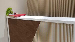 A reception desk with a white top and a brown lower section, a small potted plant, and a red book on the left side. - Hotel Grand Palace Inn (Mumbai)