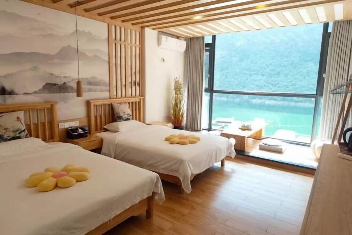 A hotel room with two beds, a large window with a view of a mountain, and a wooden ceiling.