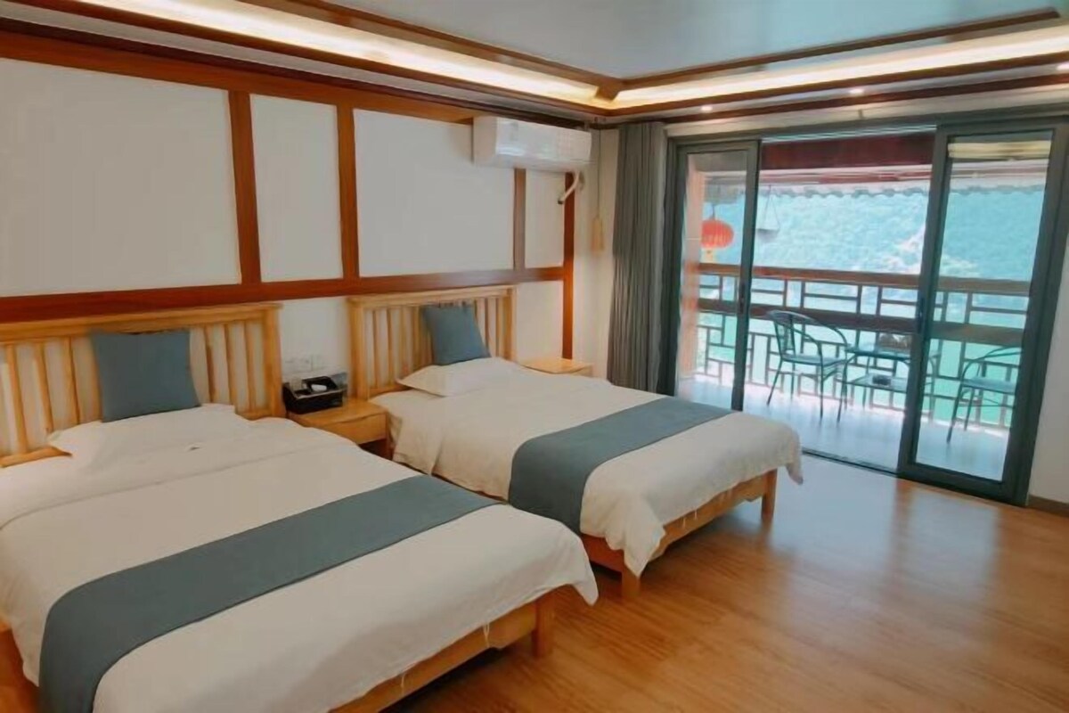 Ein Hotelzimmer mit zwei Betten, Holzböden, einem Balkon mit Sitzgelegenheiten und Meerblick.