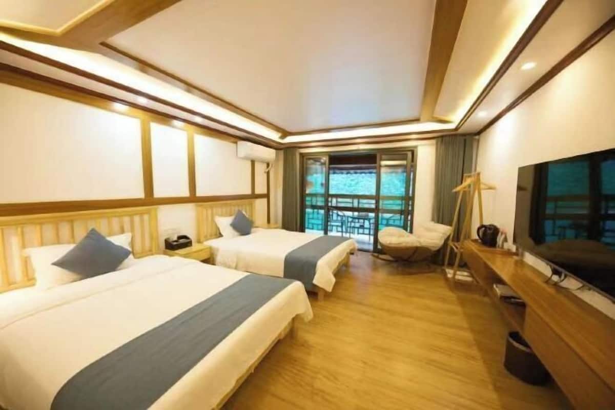 A hotel room with two beds, a TV, a desk, and a window with a view.
