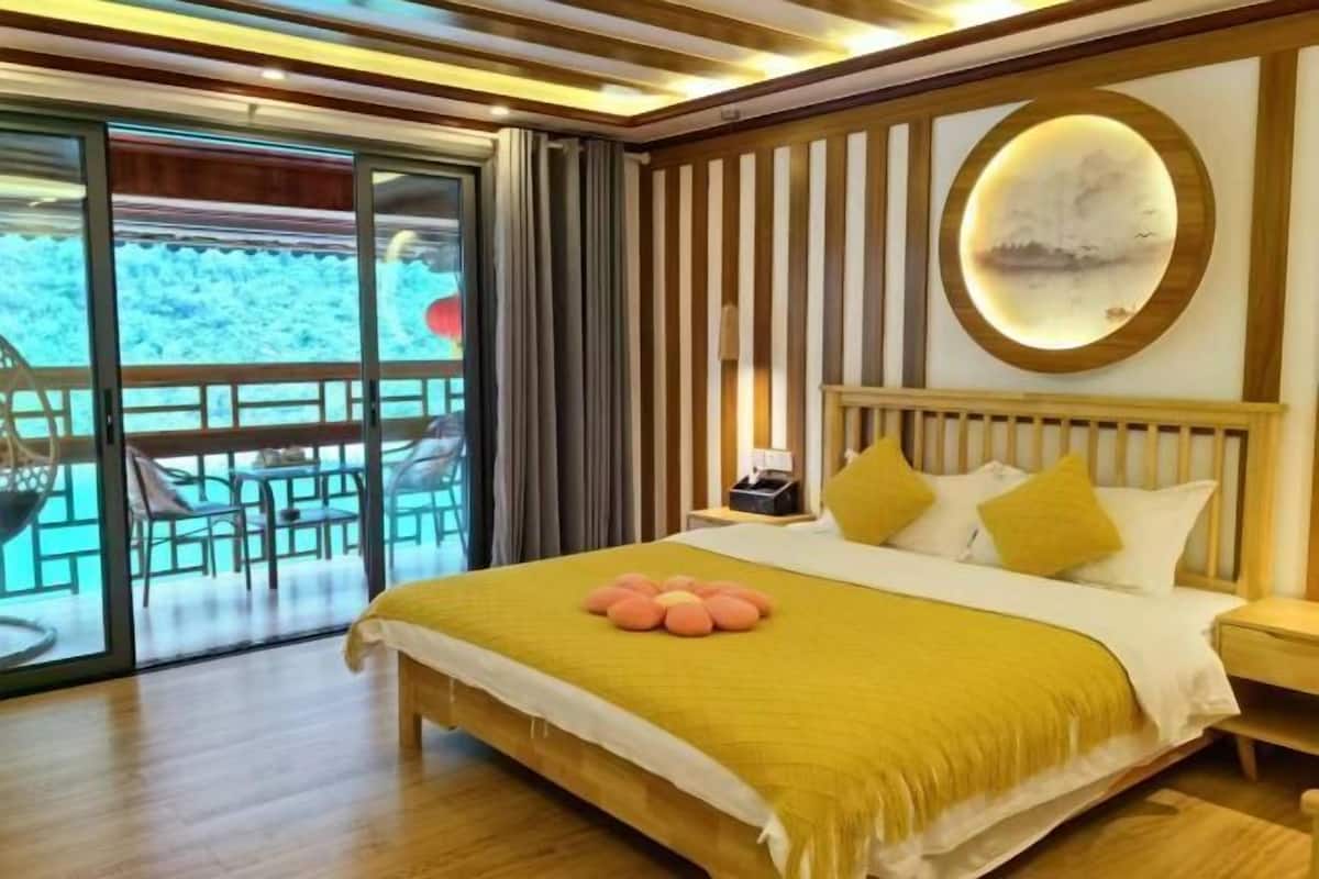 A hotel room with a bed, a nightstand, a circular wall decoration, and a view through a glass door.