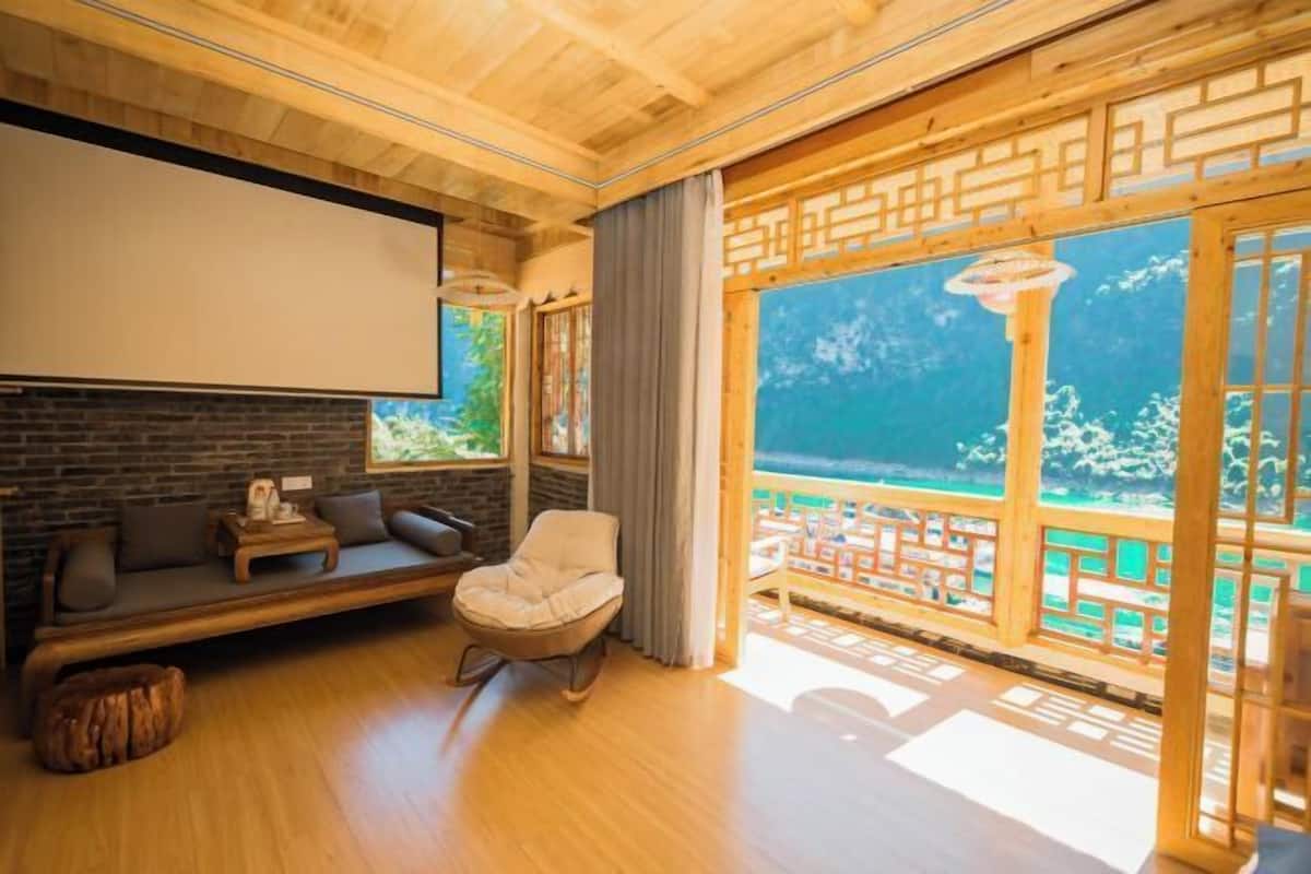 A room with a wooden ceiling, a sofa, a chair, a small table, and a large window with a view.