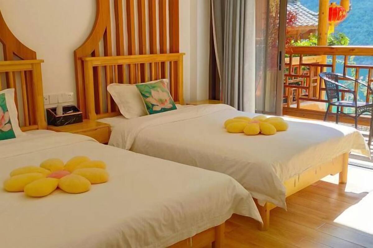 Two beds with white linens and yellow decorative pillows, wooden headboards, and a balcony with a table and chairs.