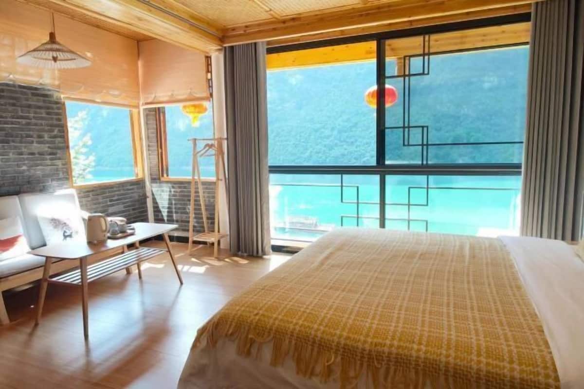 A bedroom with a bed, a desk, a chair, and a window with a view of the sea.