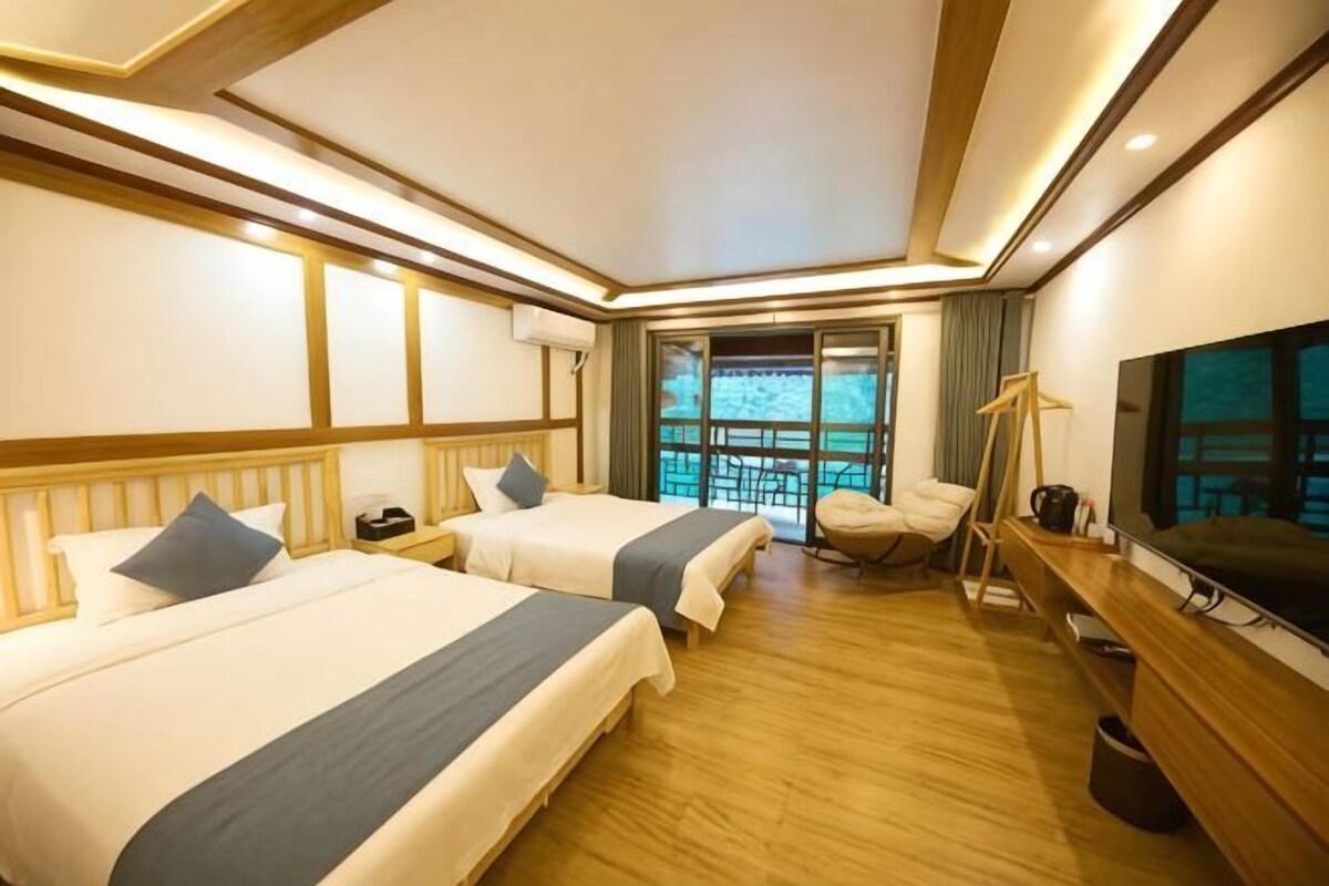 Habitación de hotel con dos camas, televisión, escritorio y balcón con vistas.