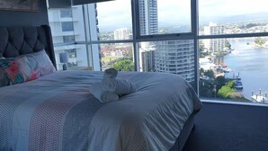 Ein Schlafzimmer mit einem großen Bett, Blick auf Stadt und Wasser, und einem Fenster mit Jalousien.
