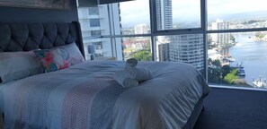 Ein Schlafzimmer mit einem großen Bett, Blick auf Stadt und Wasser, und einem Fenster mit Jalousien.