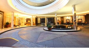 Ein mehrgeschossiges Atrium mit einer zentralen Fontäne, mehreren Etagen und einer steinernen Fassade.