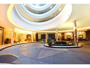 Ein mehrgeschossiges Atrium mit einer zentralen Fontäne, mehreren Etagen und einer steinernen Fassade.