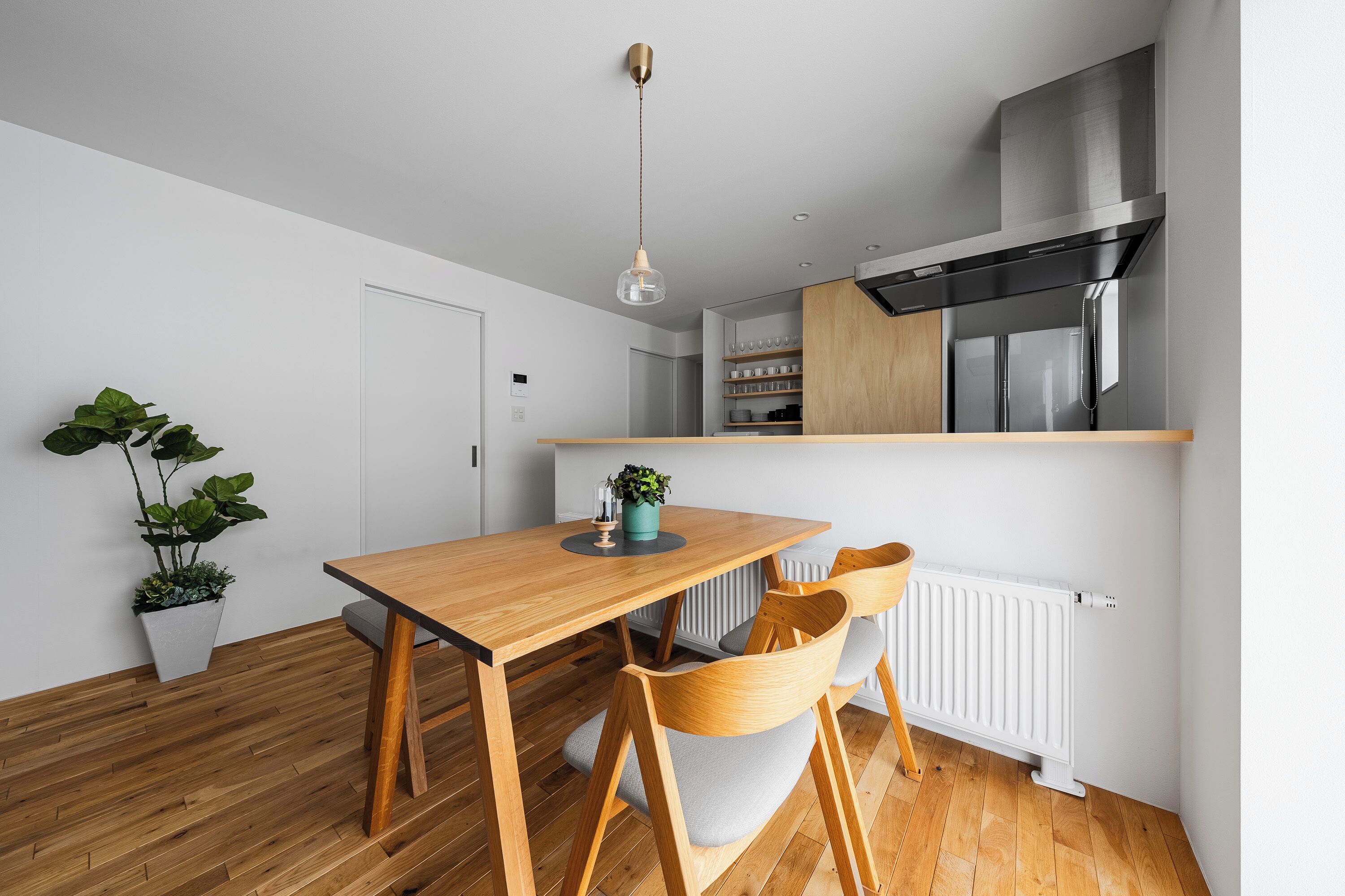 A modern kitchen with a wooden table, chairs, a hanging light, and a white radiator.