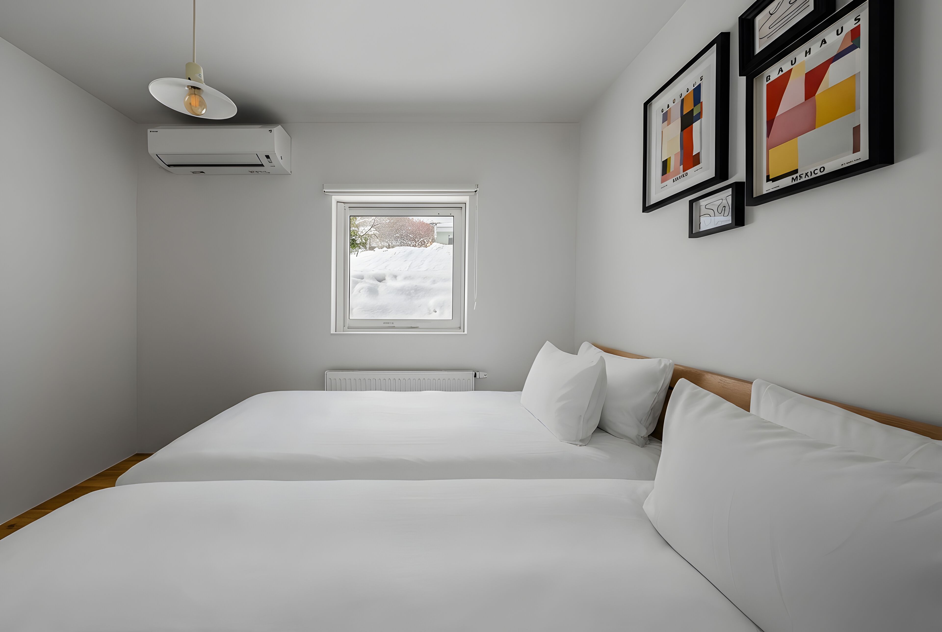A bedroom with a bed, an air conditioner, a window, and framed pictures on the wall.