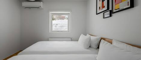 A bedroom with a bed, an air conditioner, a window, and framed pictures on the wall.