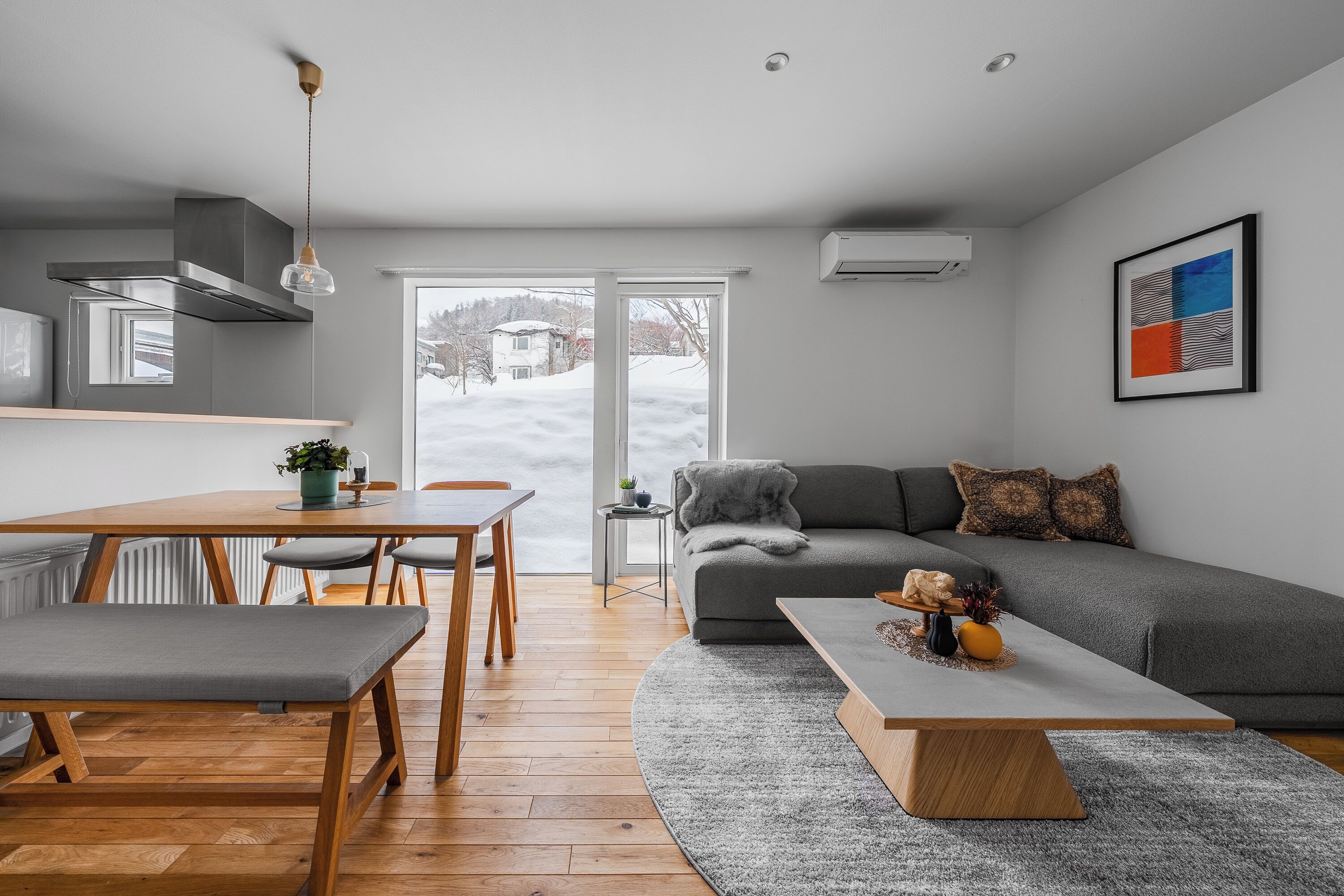 A modern living room with a grey sofa, a wooden dining table, and a grey rug.