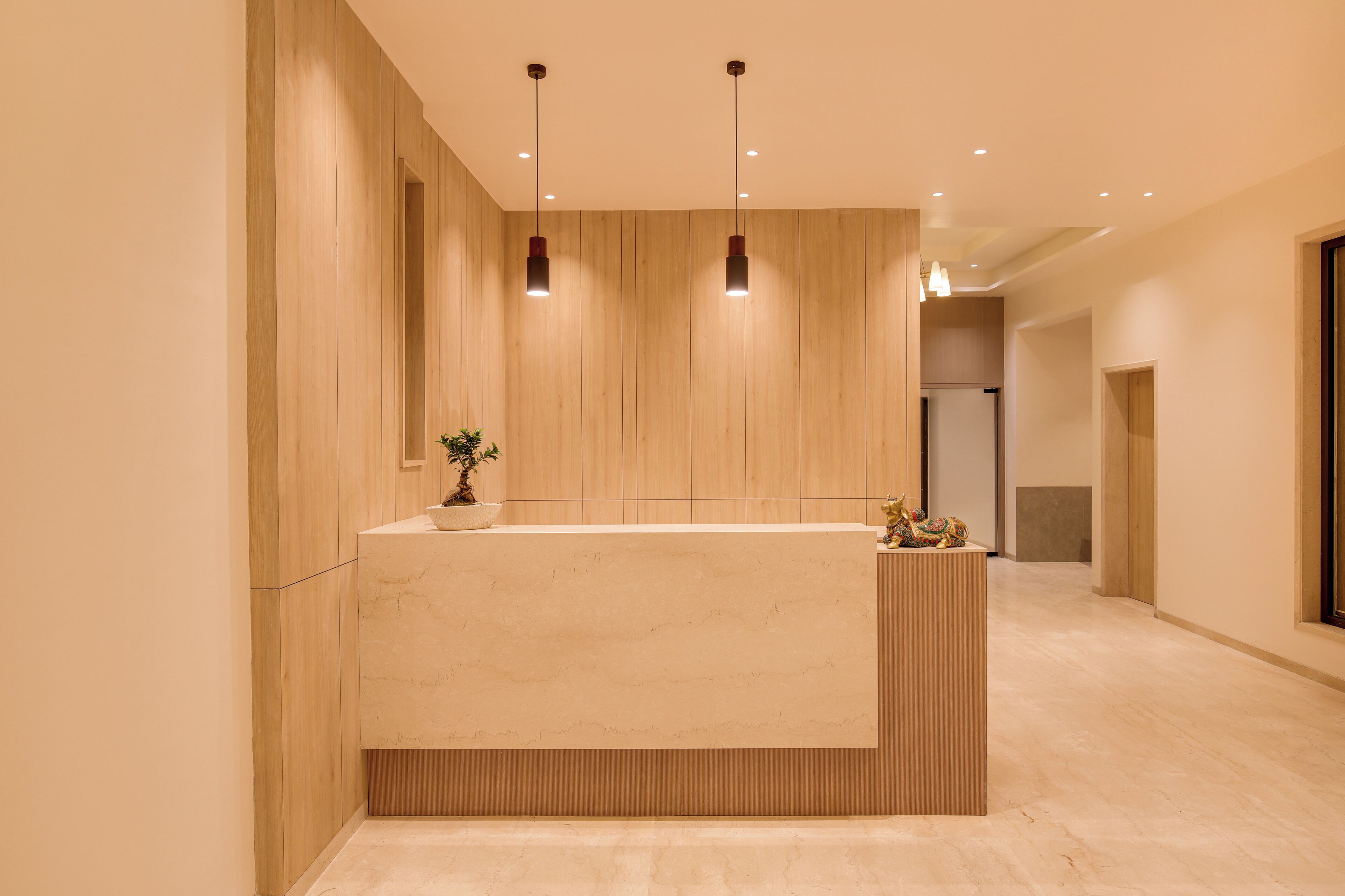 A modern reception area with a marble counter, wooden panel walls, and pendant lighting.