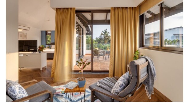 En moderne stue med sofaarrangement, et sofabord med brætspil og udsigt til en balkon med havemøbler.
