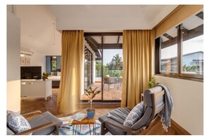 Ein modernes Wohnzimmer mit einer Sofagarnitur, einem Couchtisch mit Gesellschaftsspielen und Blick auf einen Balkon mit Gartenmöbeln.