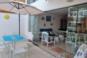 A modern living room with a glass partition, a dining area with a blue table, and white furniture.