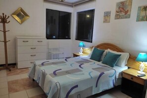 A bedroom with a bed, a dresser, two bedside tables with lamps, and a window.