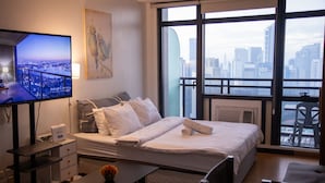 A hotel room with a bed, a desk, a chair, a TV, and a large window with a city view. - [KStayC]Studio,Best Sunset Pool/Luxury&Hotel Style (Makati)