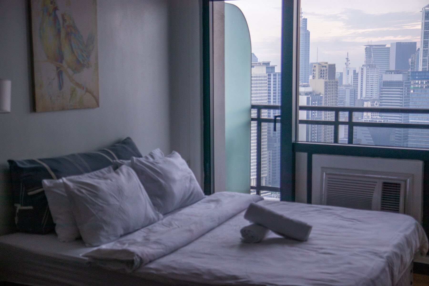 Ein Hotelzimmer mit einem Bett, Kissen, einer Decke und Blick auf eine Stadtlandschaft durch ein Fenster.