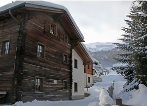 Une cabane en bois dotée d’un balcon, entourée de paysages enneigés et offrant une vue sur les montagnes.