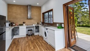 A modern kitchen with a built-in washing machine, wooden flooring, and a large window. - Cabin 2 - Accessibility, pet-friendly, adults only (Lowanna)