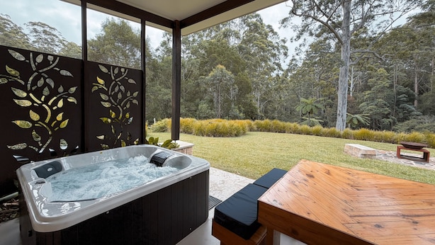 A hot tub with a wooden table and chairs, surrounded by a garden with various plants and trees. - Cabin 2 - Accessibility, pet-friendly, adults only (Lowanna)