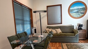 A modern living room with a glass dining table, green chairs, a grey sofa, and a round picture frame on the wall. - Cabin 2 - Accessibility, pet-friendly, adults only (Lowanna)