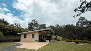 A two-story house with a covered patio, surrounded by a well-maintained lawn and dense trees. - Cabin 2 - Accessibility, pet-friendly, adults only (Lowanna)