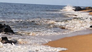 A beach with waves crashing onto the shore, a clear sky, and a calm sea.