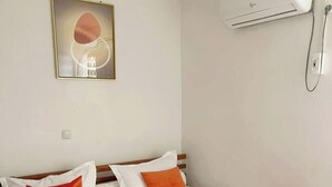 A hotel room with a bed, pillows, a blanket, an air conditioning unit, and a framed picture on the wall.