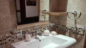 A bathroom with a white sink, wooden vanity, and a mirror above it. There are tiled walls and a mosaic backsplash. - VILLA L'OLIVIER (Kelibia)