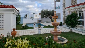 A courtyard with a fountain, a swimming pool, and a white building with a red roof. - VILLA L'OLIVIER (Kelibia)