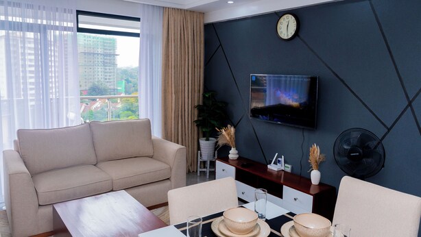 A modern living room with a sofa, coffee table, dining table, and a TV mounted on the wall. - Serene Executive 1BR in Upscale Kileleshwa (PQ9M+R3 Nairobi)