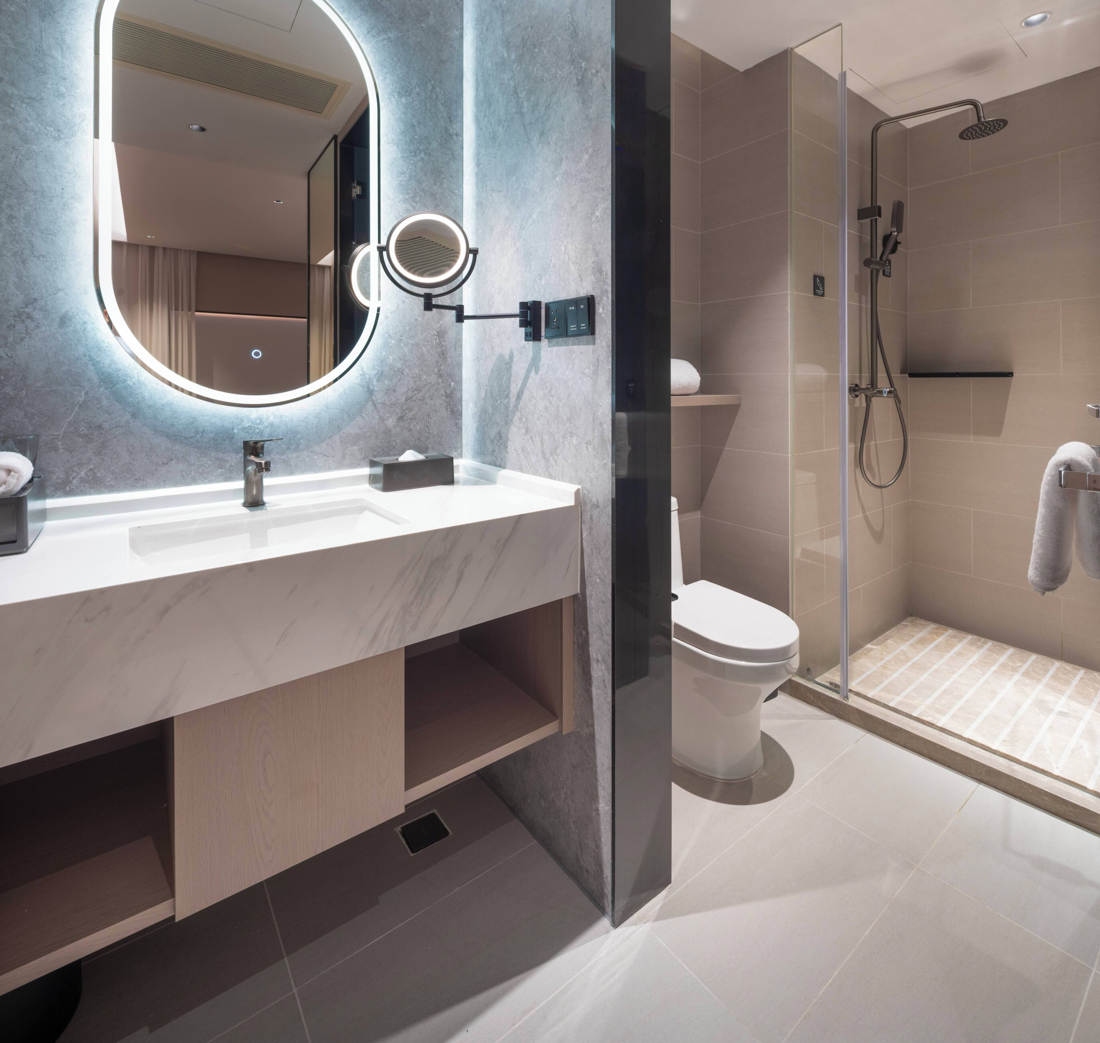 Ein modernes Badezimmer mit Marmorwaschtisch, einem großen Spiegel mit Beleuchtung, einer Toilette und einer Duschkabine.
