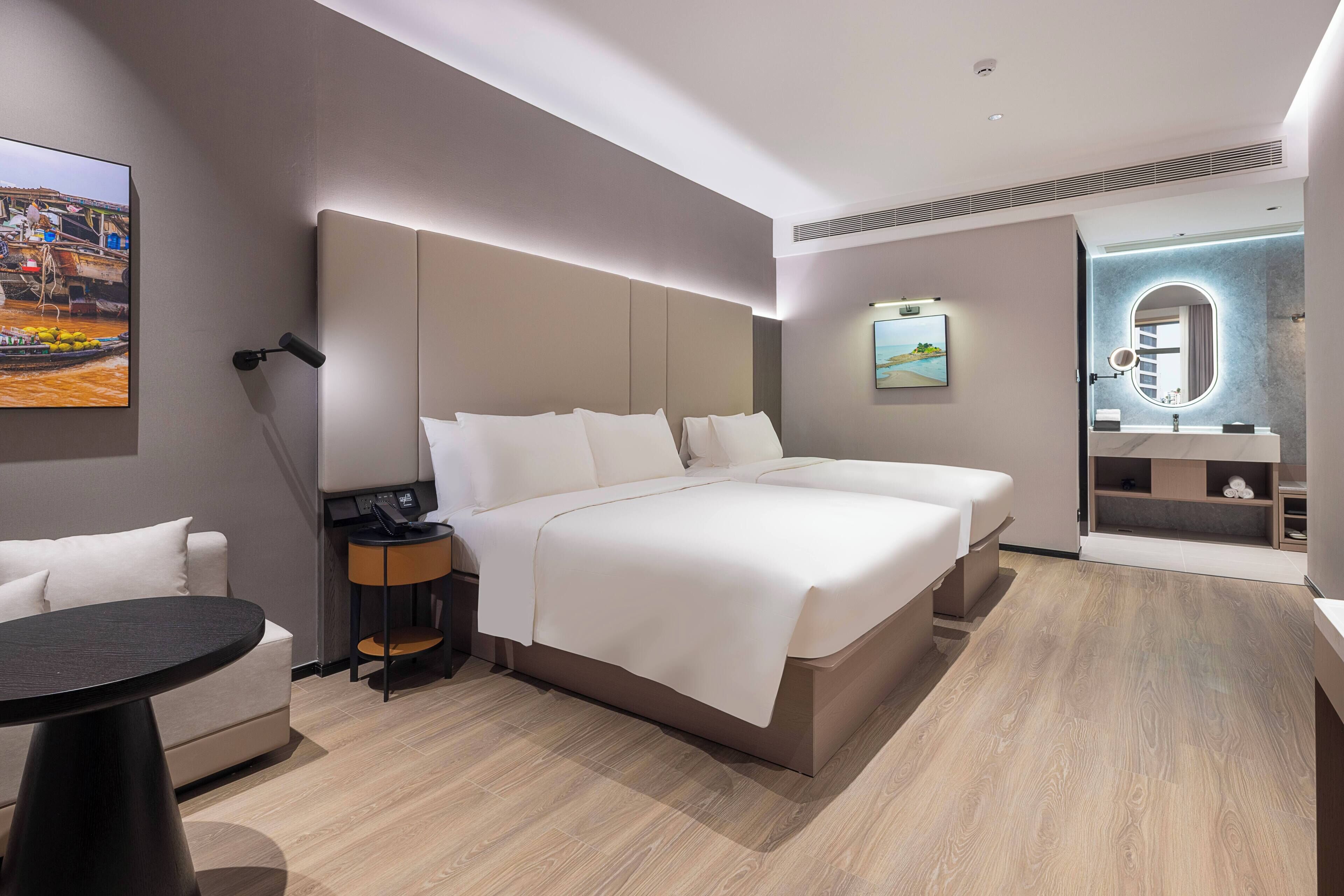 A modern hotel room with a large bed, bedside tables, a desk, and a bathroom with a vanity and mirror.