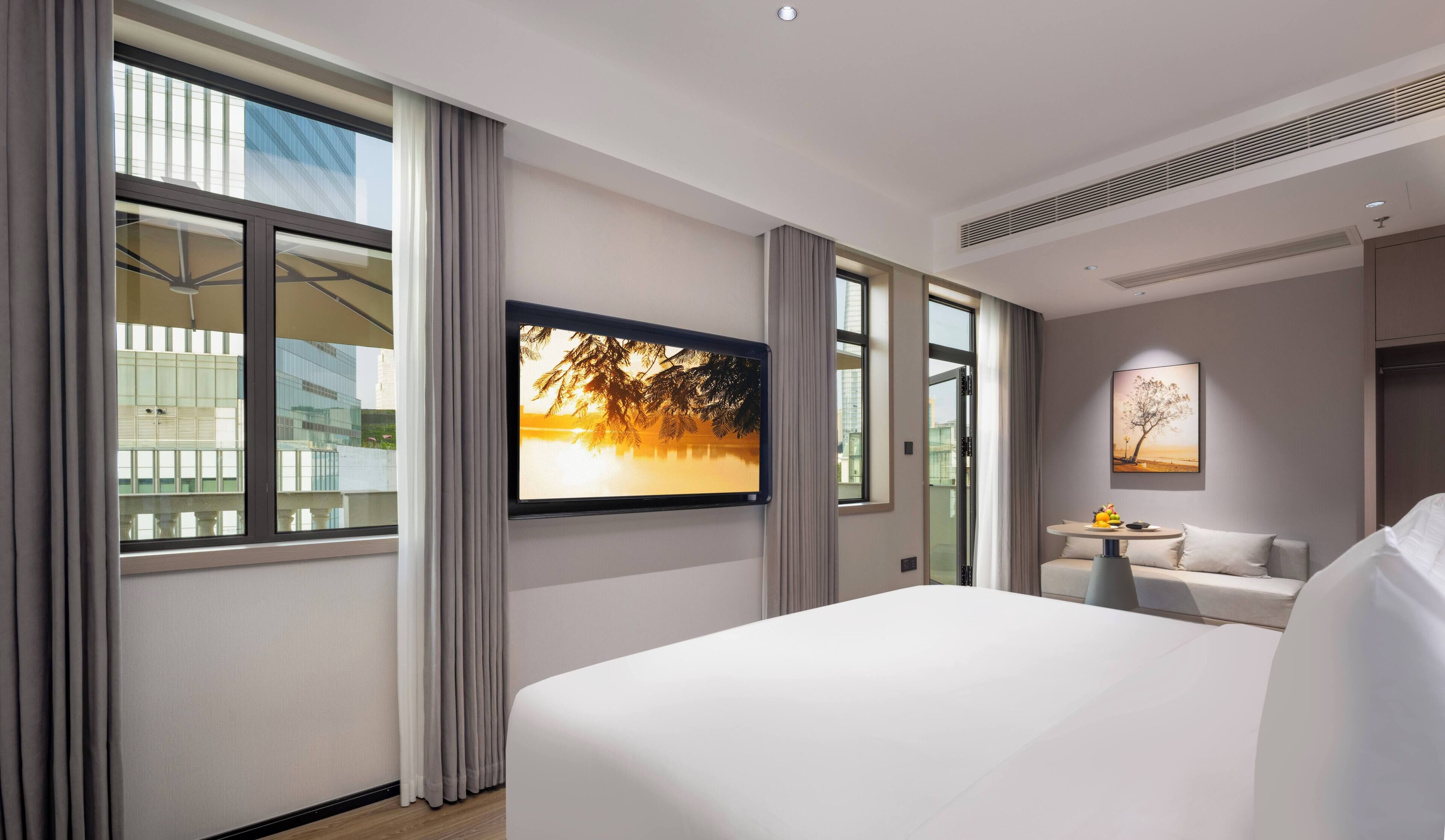 A hotel room with a large bed, a TV mounted on the wall, a small table with a vase, and a sofa.