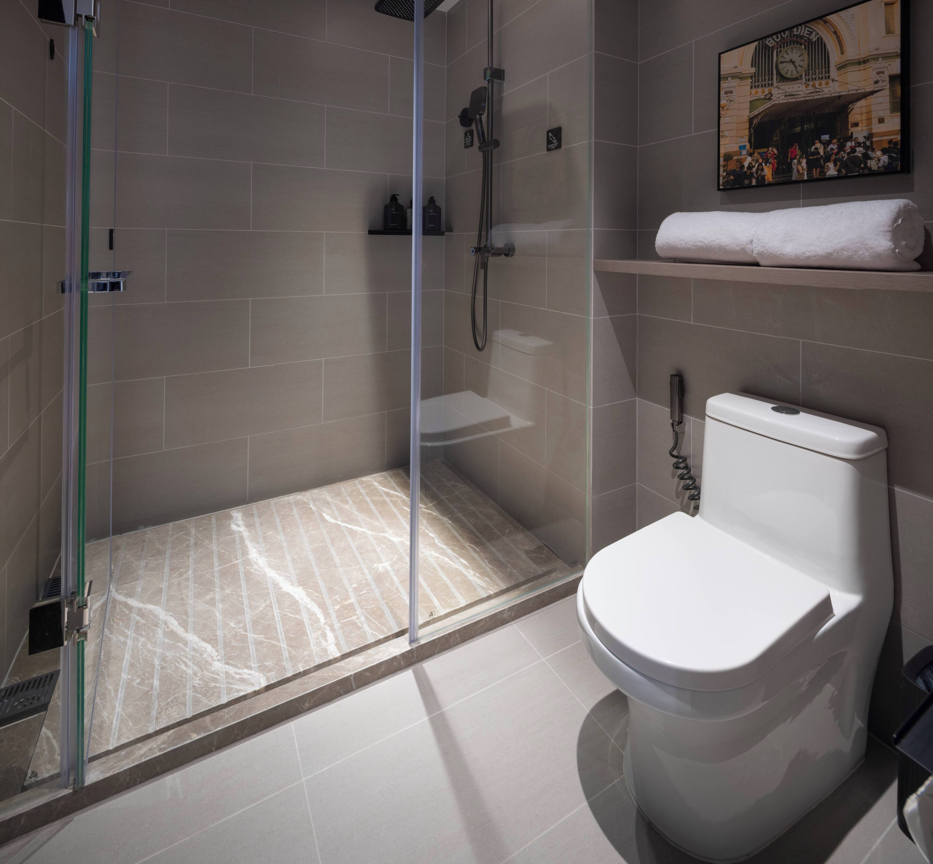 Un bagno moderno con cabina doccia in vetro, un water e uno scaffale con un asciugamano.