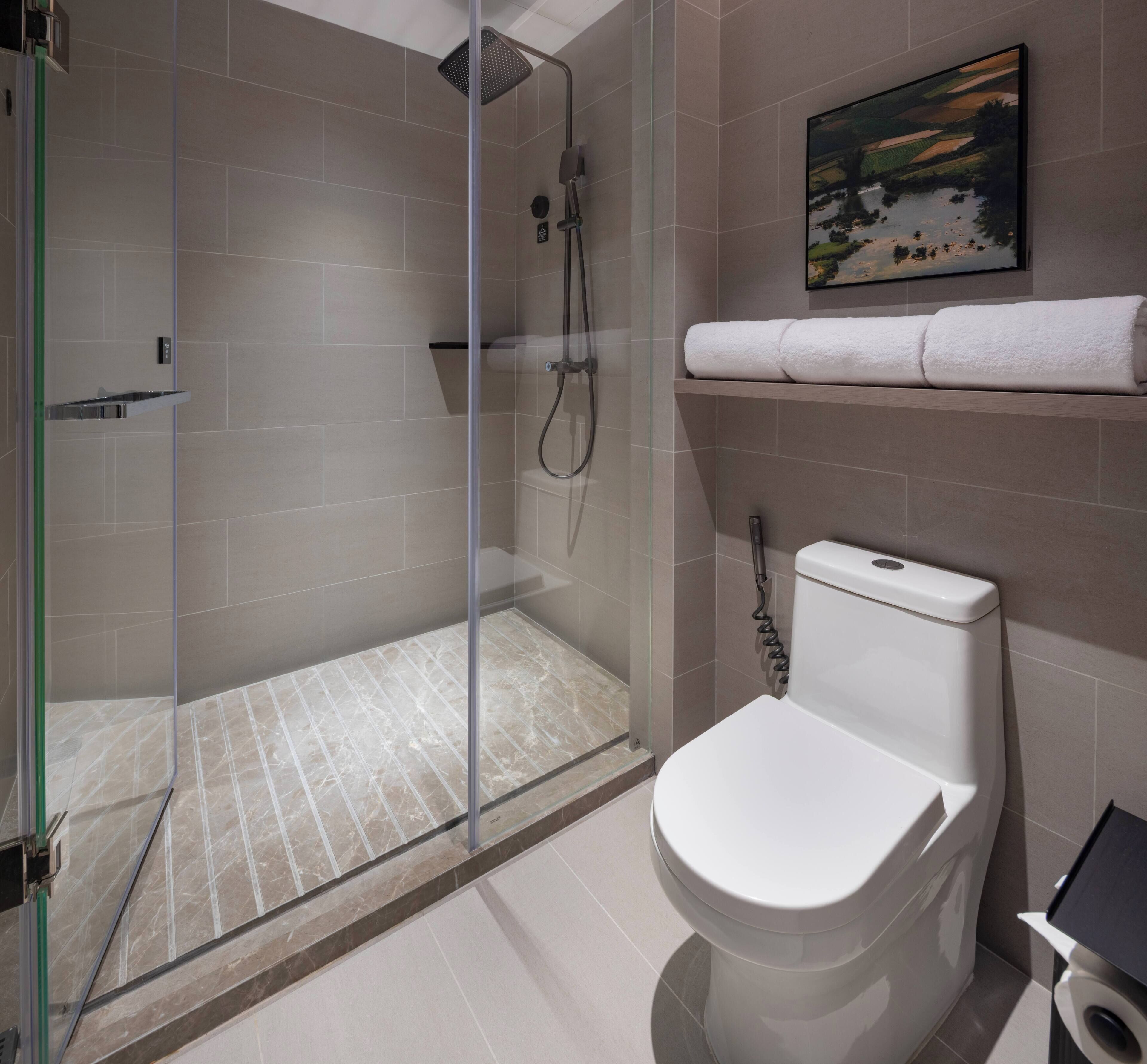 Une salle de bain moderne avec une douche à parois de verre, des toilettes et une étagère sur laquelle est posée une serviette.