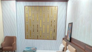 Habitación de hotel con dos camas, un sofá, una silla, una mesa de centro redonda y un panel decorativo en la pared.