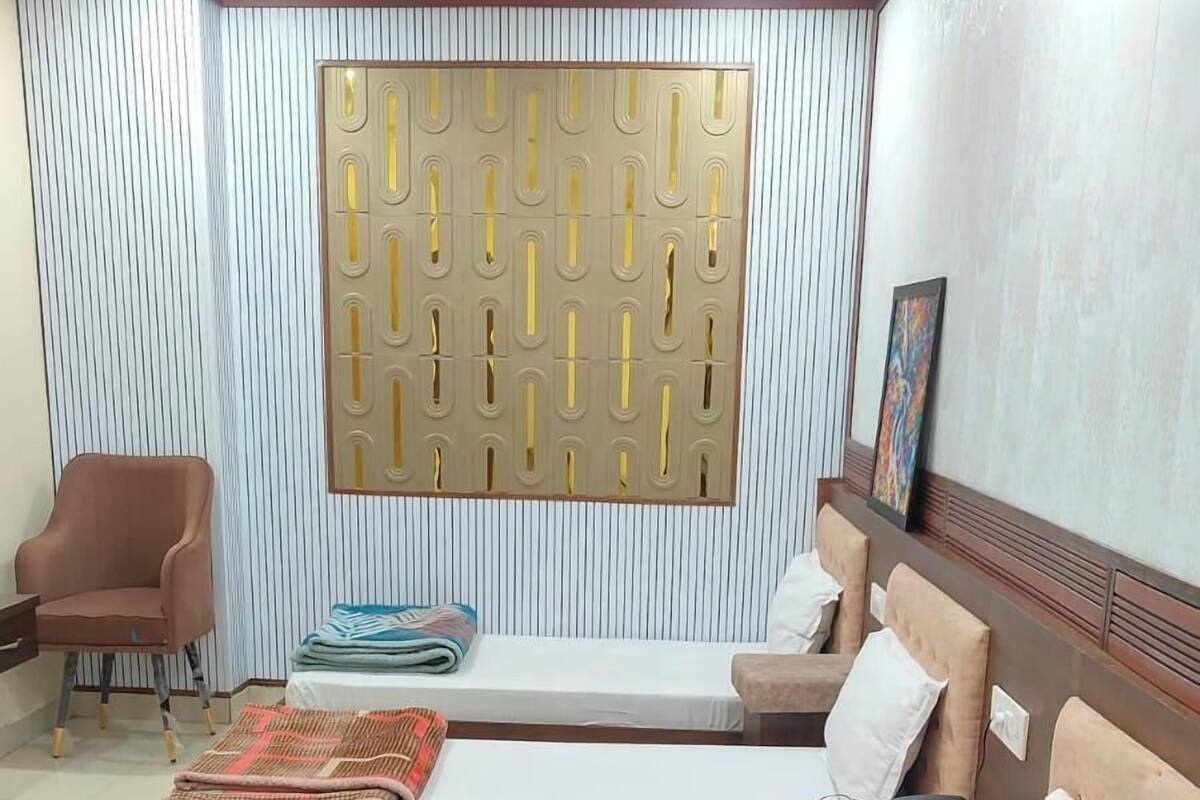 Habitación de hotel con dos camas, un sofá, una silla, una mesa de centro redonda y un panel decorativo en la pared.