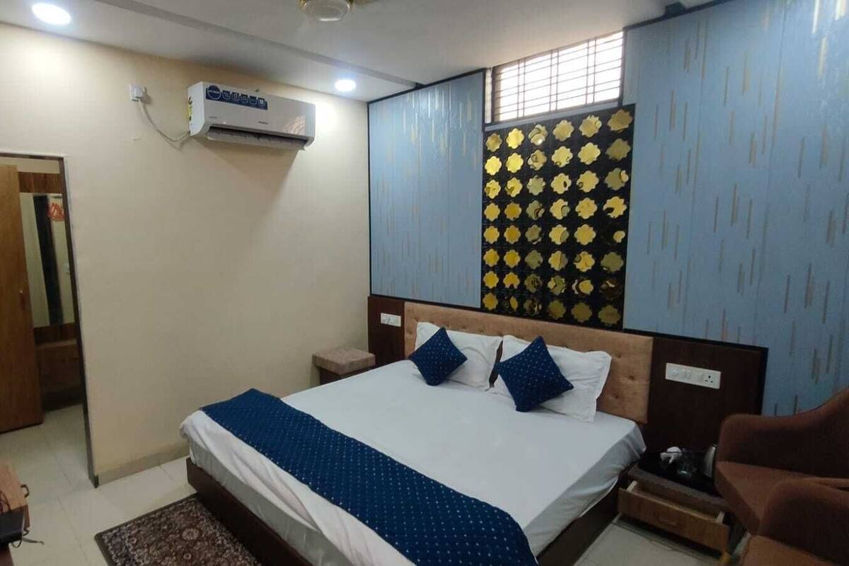 Un dormitorio con cama, mesitas de noche, un equipo de aire acondicionado, un papel tapiz decorativo y una puerta.