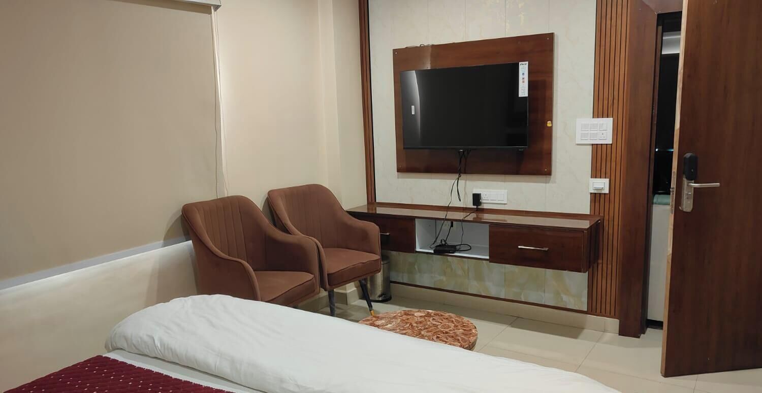 Habitación de hotel con cama, dos sillones, televisor montado en un mueble de madera y puerta que da a otra habitación.