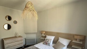 A bedroom with a bed, a wooden headboard, a bedside table, a radiator, and a hanging light fixture.