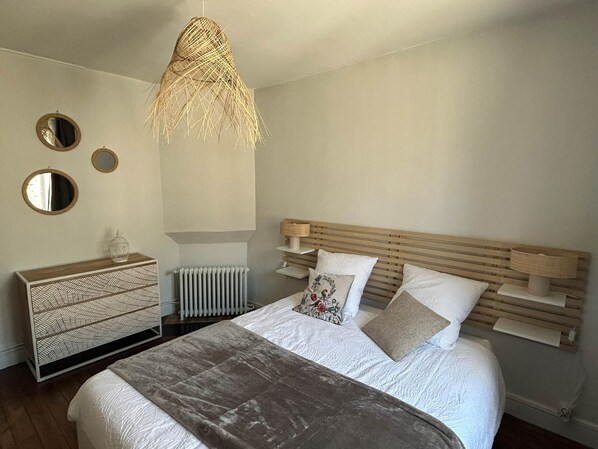A bedroom with a bed, a wooden headboard, a bedside table, a radiator, and a hanging light fixture.